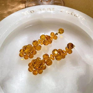 Macro shot of amber crystal flower earrings on a white tray with golden fabric