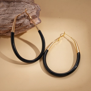 Close-up of gold and black oval hoop earrings with hinged clasp on a wooden base