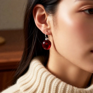 Close-up of deep red apple pendant earring worn with a beige chunky knit sweater