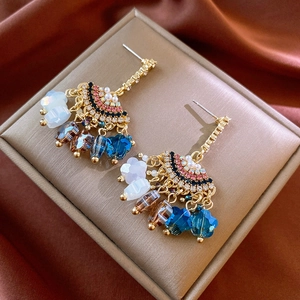 Detail of vintage gold fan-shaped earrings with colorful crystal tassels on silk background