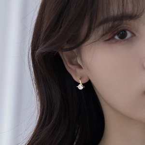 Close-up of gold geometric oval earring with a small white pearl drop on a female model