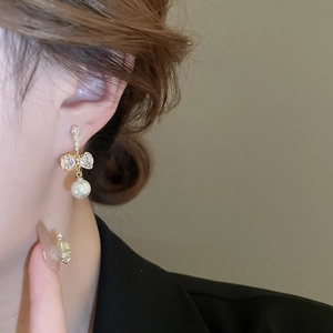 Boucles d'oreilles nœud dorées avec zircon et perles portées par un mannequin chic