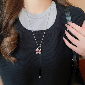 Detail of silver Y-shaped necklace with a red floral pendant on a black sweater