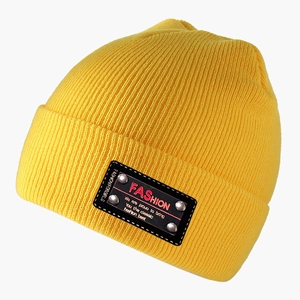 Close-up of yellow ribbed knit beanie featuring a black patch with silver metal rivets