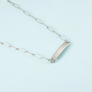 Detailed macro view of polished silver rectangle bar pendant on a paperclip chain necklace