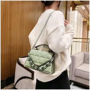 Detail of light green quilted handbag featuring chunky chain and fine shoulder strap