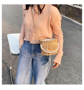 Close-up of woven straw bucket bag with pearl handle and golden chain shoulder strap