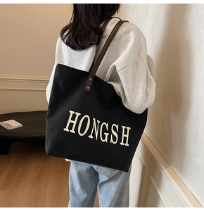 Close-up of black canvas tote bag with white lettering on model in a soft minimalist room