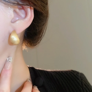 Close-up of matte gold teardrop earring with brushed metal finish on model