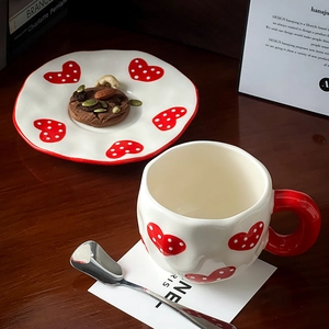 Close-up of ceramic coffee cup and saucer with red heart pattern and wavy edges