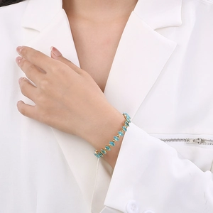 Close-up of golden bangle with marquise-cut teal stones on female wrist with white suit