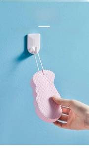 Pink exfoliating bath sponge with wavy texture and white lanyard hanging on a wall hook