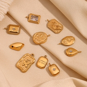 Detailed close-up of 18K gold plated charms with rose engraving on beige silk fabric