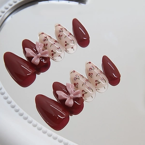 Deep burgundy and cherry print almond press-on nails with 3D pink bows on a pearl mirror