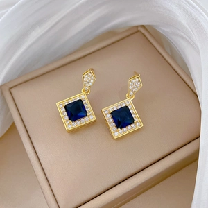 Macro shot of gold-plated square earrings with deep blue stones and zircon pavé