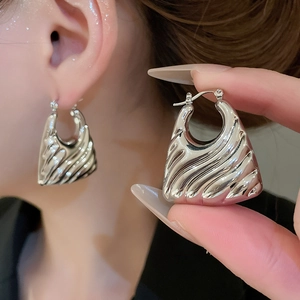 Macro shot of silver chunky hoop earrings featuring modern textured ripple wave design