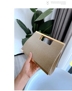 Detail of beige woven clutch bag with gold metal handle held in a modern setting