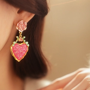 Macro view of pink rose stud with glittering heart pendant earring on female model