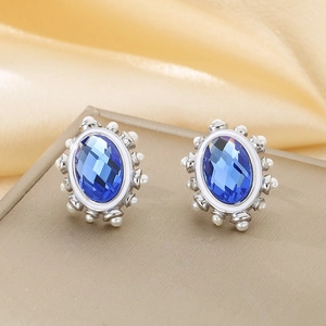 Macro shot of oval blue crystal earrings with white bead inlay on silk background