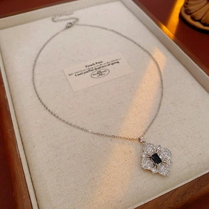 Detail of silver clover necklace with black gem and pavé diamonds on a wooden tray