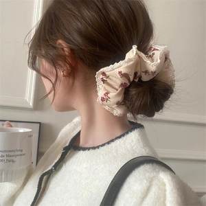 Close-up of beige floral scrunchie with red flowers and lace trim on model's wrist