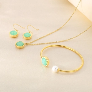 Detail of gold jewelry set with green circular stones and white pearl on beige fabric