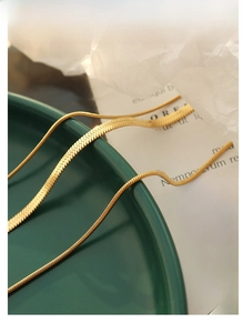 Detailed close-up of golden flat snake chain necklace on green ceramic plate