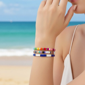 Three bohemian colorful enamel tile tila bead bracelets worn on a beach background
