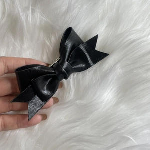 Detail of glossy black leather bow hair clip held by hand against a white plush background