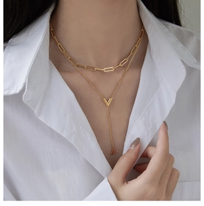 Detailed view of layered 18K gold plated V pendant necklace on a white shirt model