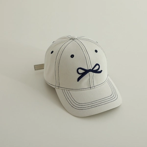 Détail de la casquette blanc cassé avec nœud brodé bleu marine et surpiqûres bleues