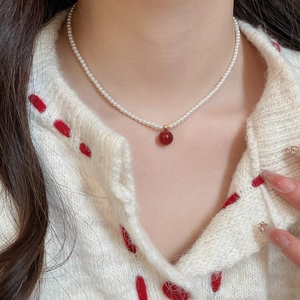 Detail of pearl necklace with red agate pendant worn by model on white knit sweater