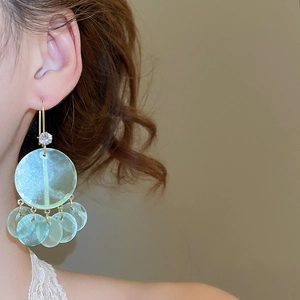 Close-up of mint green shell earrings with zircon studs worn by a model in soft light