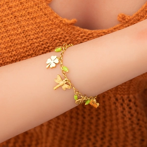 Detail of 18K gold bracelet featuring clover, dragonfly charms and green beads on a wrist