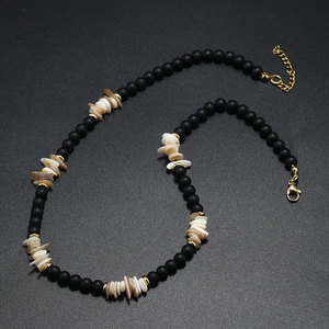 Détail d'un collier bohème avec perles noires mates, coquillages et fermoir doré