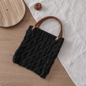 Detail of black knit tote bag showing cable knit texture and brown wooden handle
