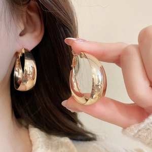 Close-up of chunky golden hoop earrings with mirror polish finish on model's ear