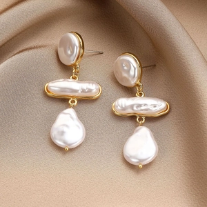 Macro detail of baroque pearl drop earrings featuring gold trim on champagne silk fabric