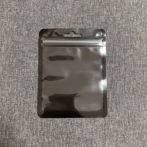 Glossy black plastic self-sealing pouch with hang hole detail on grey textured fabric