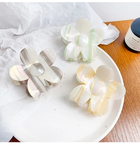 Detailed view of pearlescent floral hair claws in iridescent colors on ceramic plate