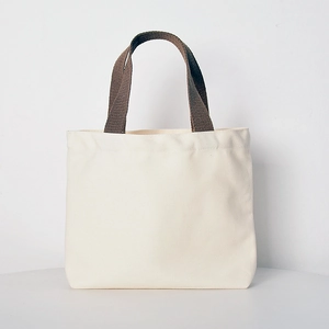 Detail of off-white canvas tote bag featuring brown woven handles and premium fabric texture