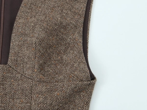 Dettaglio del tessuto tweed marrone con trama intrecciata e macchie arancioni sull'abito