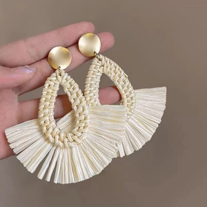 Detail showing handmade woven raffia teardrop earrings with golden circular metal studs