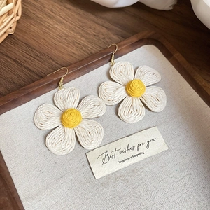 Detail of flower-shaped resin woven earrings with cream petals and yellow centers