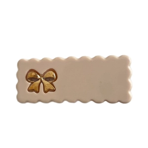 Barrette à cheveux beige ondulée avec un nœud doré sur un fond blanc épuré