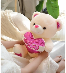 Detail of plush teddy bear holding a metallic pink heart with LOVE embroidery in soft fabric