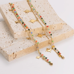 Double-layered gold bracelet with colorful beads and star charms on travertine stone