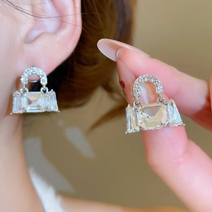 Detailed close-up of sparkling silver handbag-shaped earrings with inlaid crystals