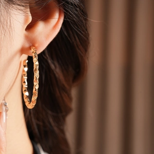 Close-up of golden geometric faceted C-shaped hoop earrings worn by a model