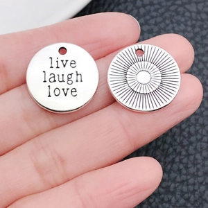 Detailansicht der silbernen Anhänger mit Live-Laugh-Love-Gravur auf der Hand